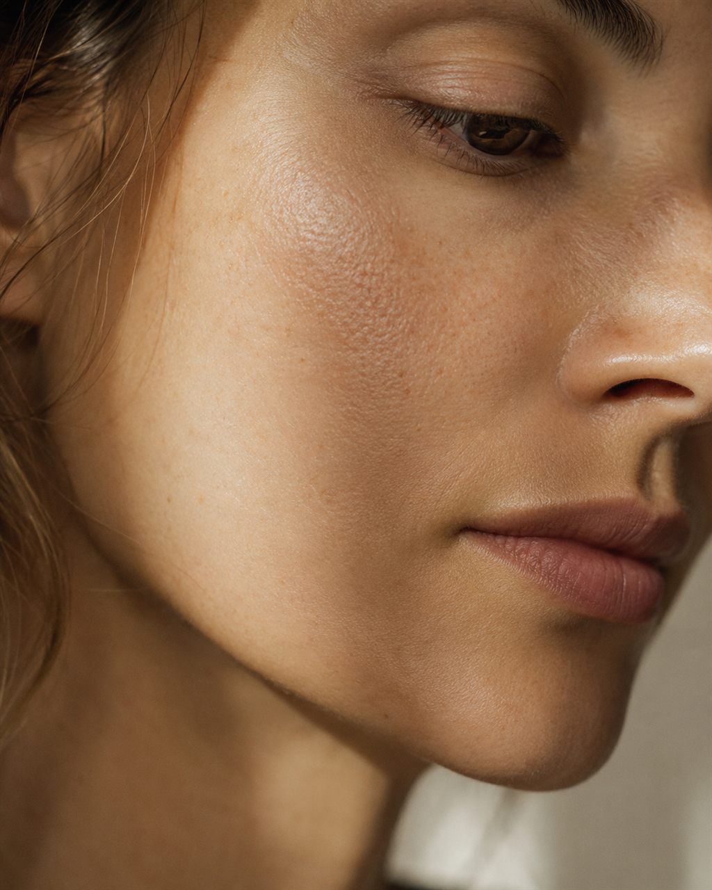 Profile of a woman in her thirties, skin texture in soft light. Illustrative image — not a patient.